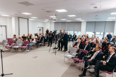 Na tle głównym sala konferencyjna z uczestnikami spotkania.